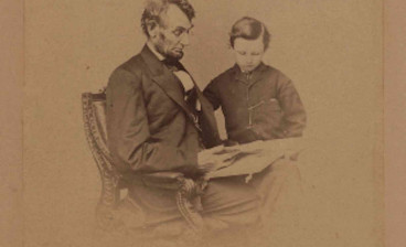 Original portrait photograph of Lincoln seated with a book and his son Tad, taken February 9, 1864