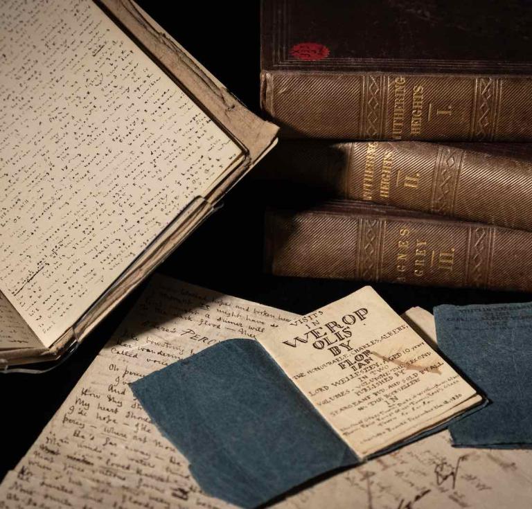 An arrangement of items on display. Top left: Fireside Tales by Charlotte Brontë; top right: first edition of Wuthering Heights and Agnes Grey by Emily and Anne Brontë; bottom right: Visits in Verreopolis by Charlotte Brontë; underneath: autograph letters by Branwell Brontë. 