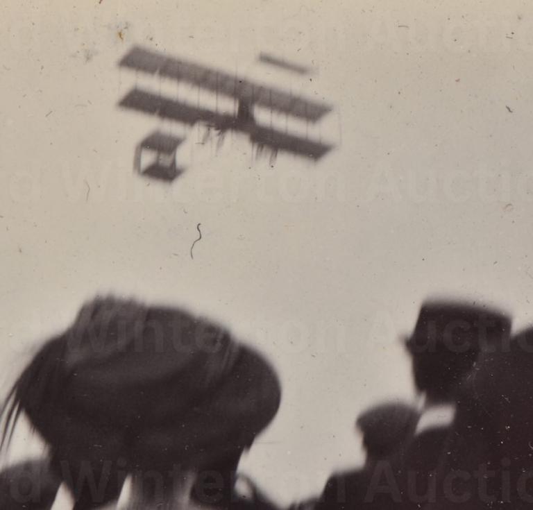 A crowd watches an early aircraft in flight