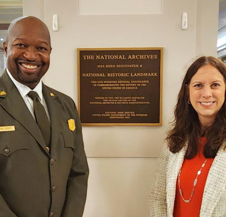 Archivist of the United States Dr. Colleen Shogan (right) and Brian Joyner, acting superintendent of Rock Creek Park (left), stand in front of the National Archives Building Historic Landmark plaque.